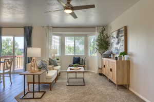 Living area featuring a ceiling fan with integrated lighting, a bay window with blinds, and a sliding glass door leading to a deck