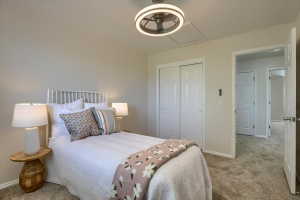 Bedroom featuring a ceiling fan with integrated lighting, textured carpet flooring, and a double-door closet with white paneled doors