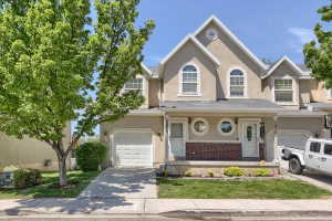 Stucco townhouse exterior featuring arched and circular windows, a covered entry with a white door, an attached garage, and a manicured lawn