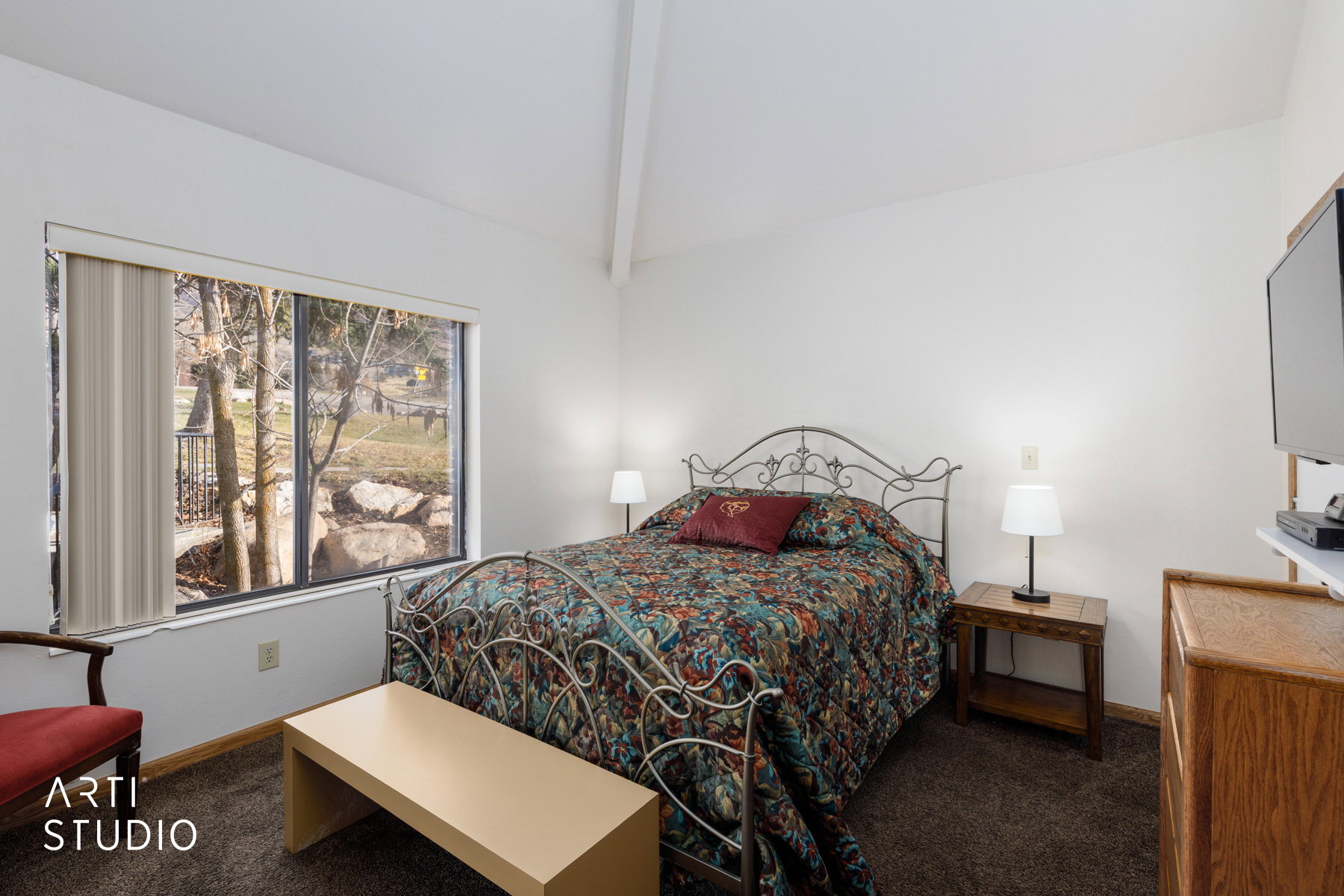 Bedroom with vaulted ceiling, large picture window, dark carpeting, and a built-in wood-finish cabinet