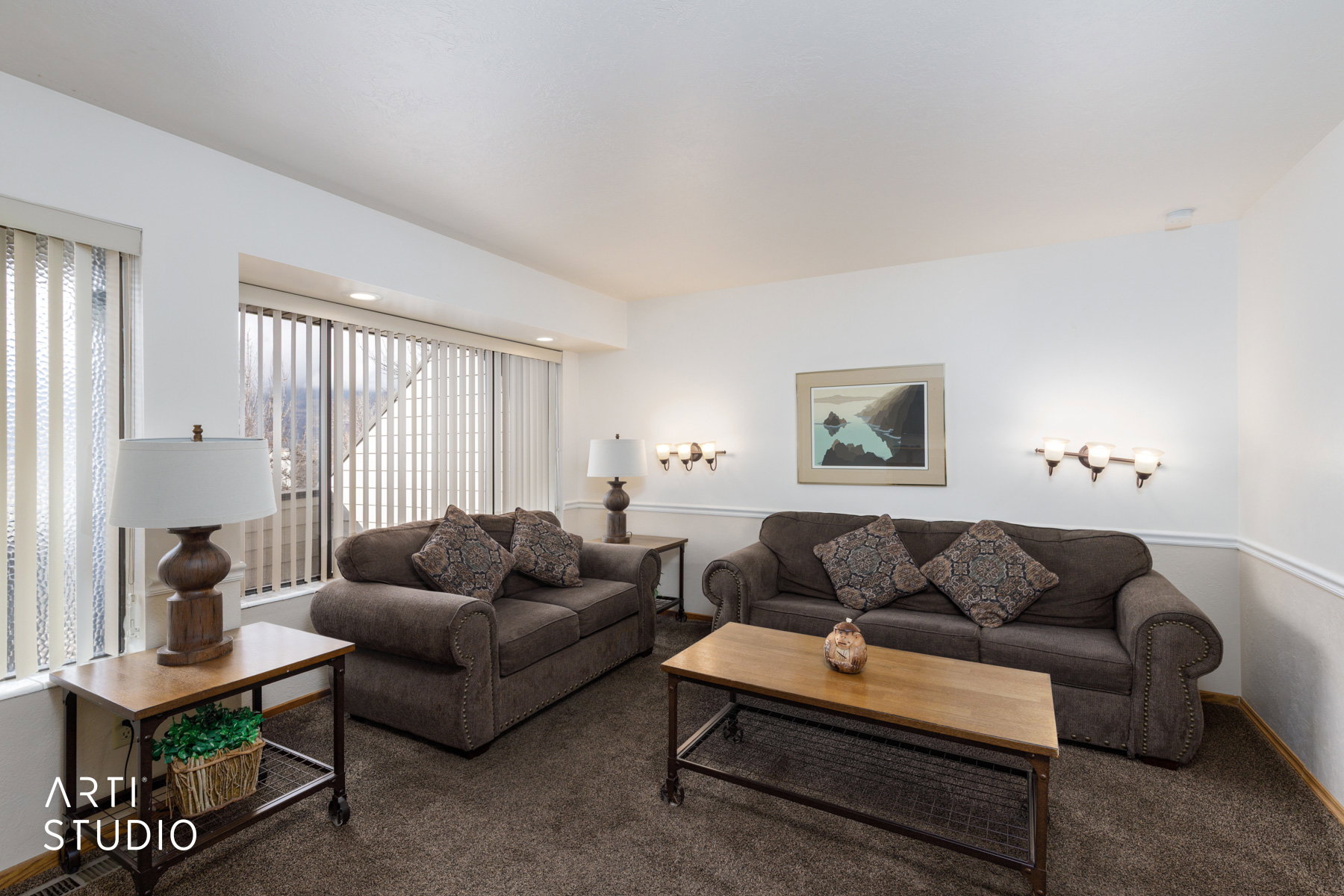 Bright living area featuring white walls, deep brown carpeting, and a large bay window