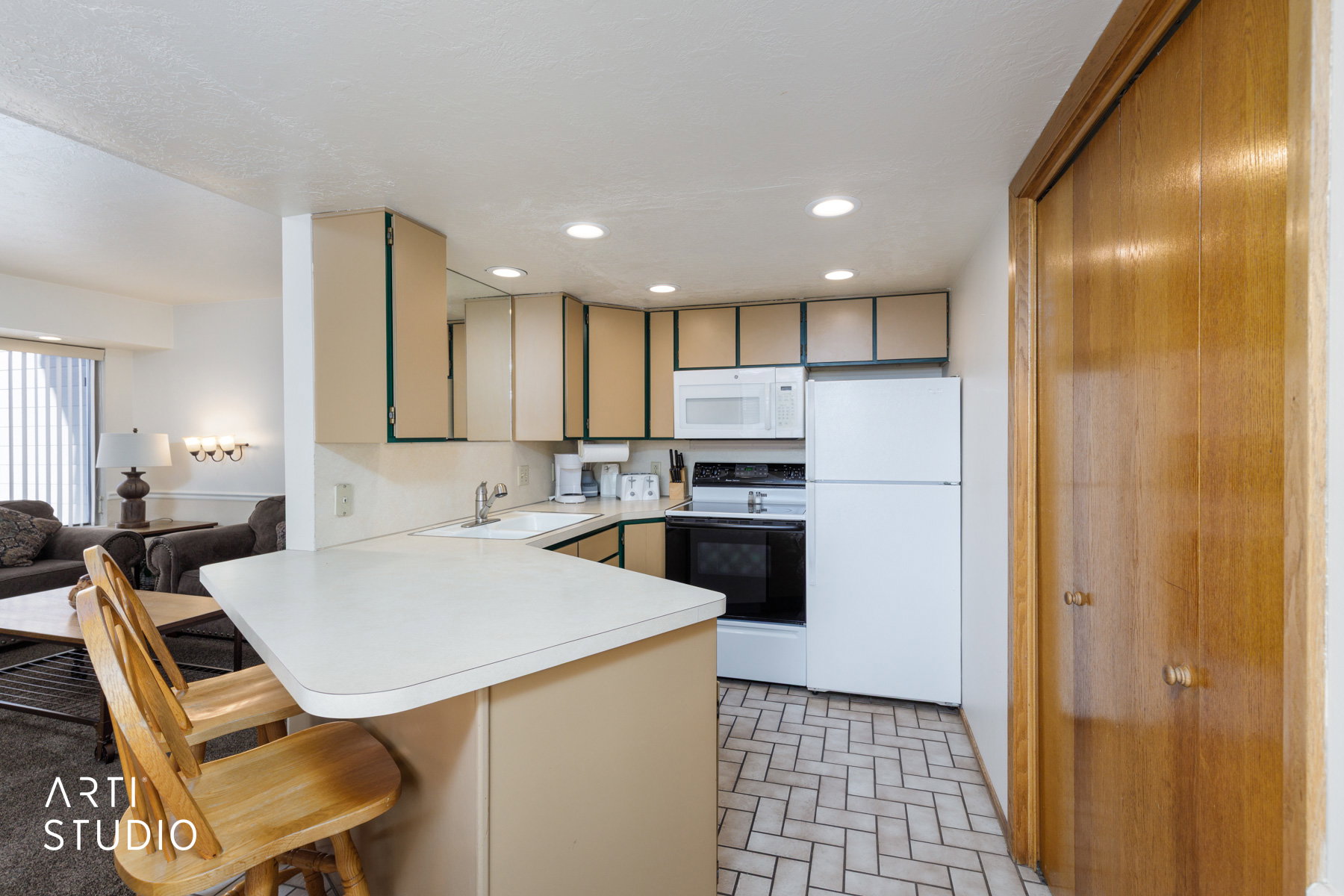 Kitchen featuring cream cabinetry, white appliances, a peninsula with counter seating, recessed lighting, and herringbone tile flooring