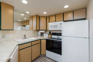 U-shaped kitchen featuring wood-finish cabinetry, white appliances, a white sink, and recessed lighting