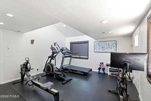 Dedicated exercise room featuring dark rubber flooring, white walls, and a vaulted ceiling