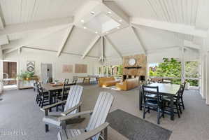 Spacious common area featuring an expansive vaulted ceiling with exposed beams, a central skylight, a stone-faced fireplace, and large windows