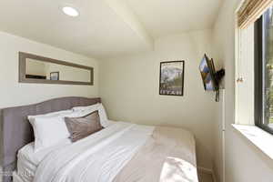 Bedroom featuring a built-in wall-mounted television, a large window with blinds, and a framed mirror