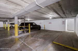 Underground parking garage featuring concrete flooring, exposed concrete ceiling, support columns with protective yellow guards, and a dedicated storage room entrance