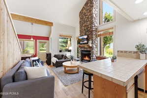 Living area featuring a floor-to-ceiling stone fireplace, vaulted ceilings, and light wood-finish flooring