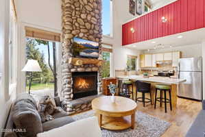 Vaulted ceiling living space featuring a floor-to-ceiling stone fireplace, natural wood mantel, and large windows