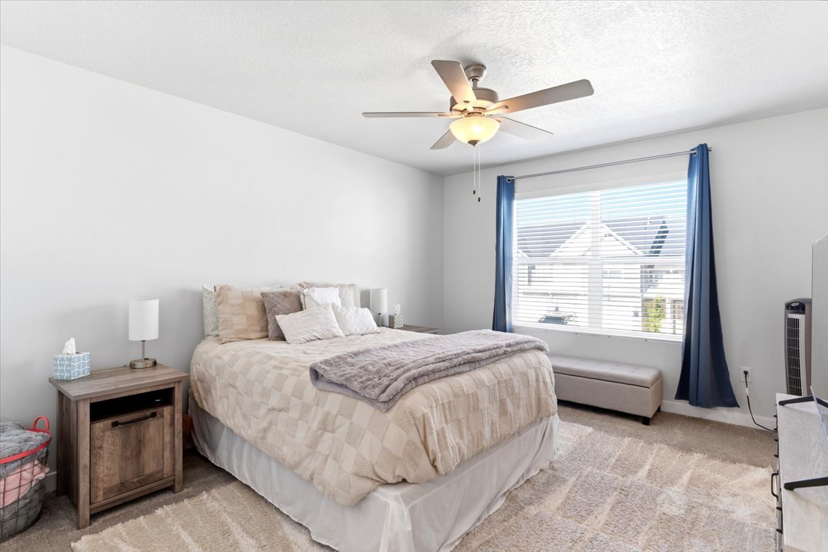 Bedroom featuring a ceiling fan with integrated lighting, a large window with blinds, and light-toned carpeting