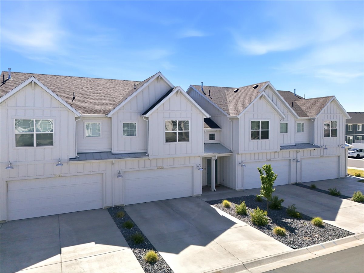 Contemporary townhome exterior featuring white board and batten siding, multiple gabled roofs, two-car garages, and concrete driveways
