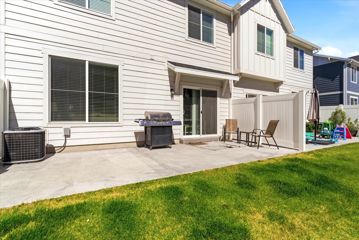 Backyard patio featuring concrete surfacing, sliding glass door access, white vinyl privacy fencing, and a manicured lawn area