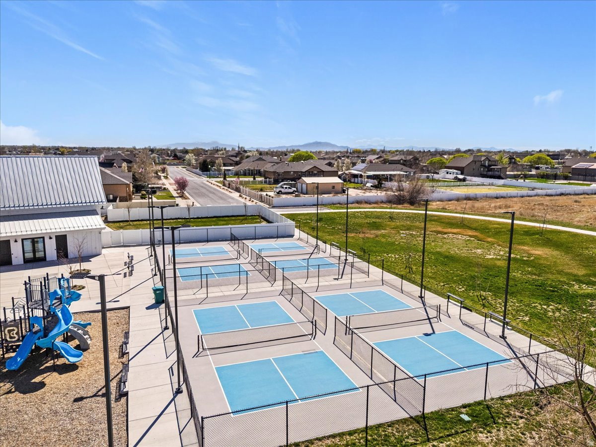 Multiple pickleball courts with black fencing, a adjacent playground featuring blue and gray structures, and a white building with a metal roof