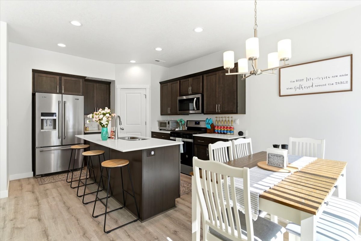 Kitchen featuring dark wood cabinetry, stainless steel appliances, a center island with a white countertop and integrated sink, and wood-finish flooring
