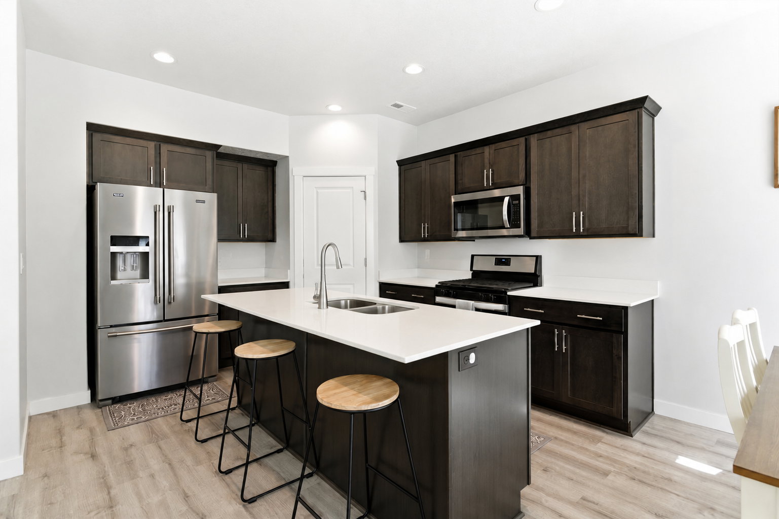 Kitchen featuring a center island with integrated sink, dark wood-finish cabinetry, stainless steel appliances, white countertops, and wood-finish flooring