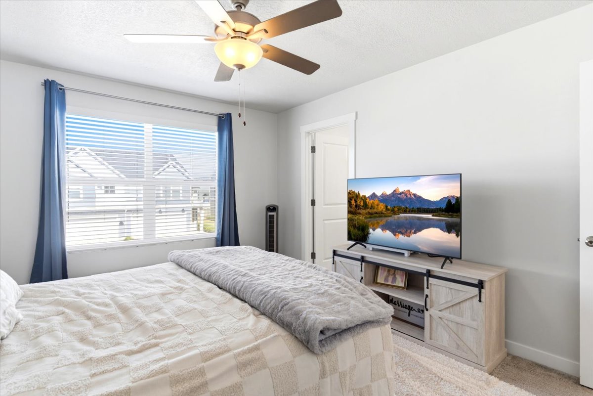 Bedroom featuring a ceiling fan with integrated lighting, large window with blinds, and light-toned carpeting