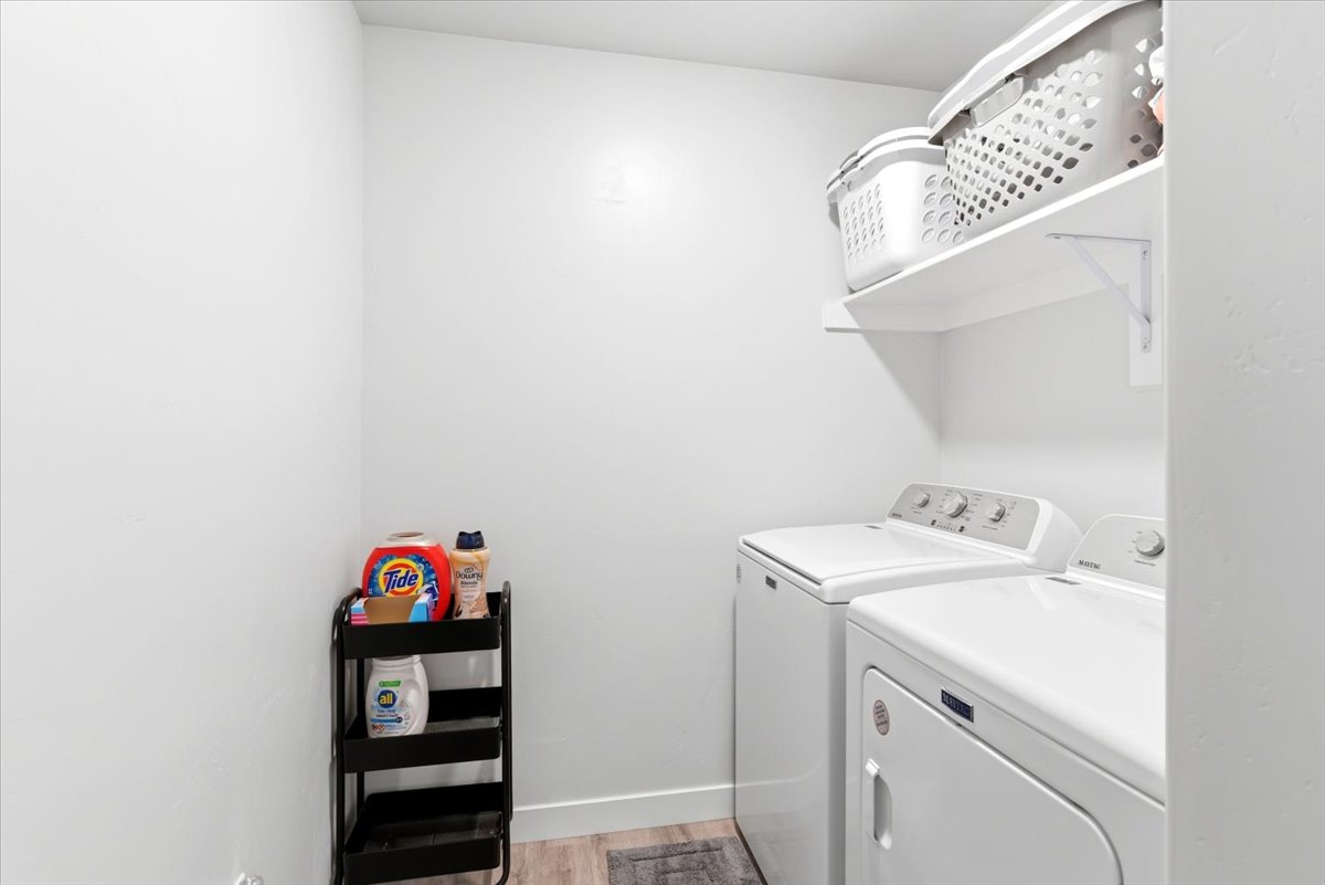 Dedicated laundry area featuring white walls, overhead shelving, and wood-finish flooring
