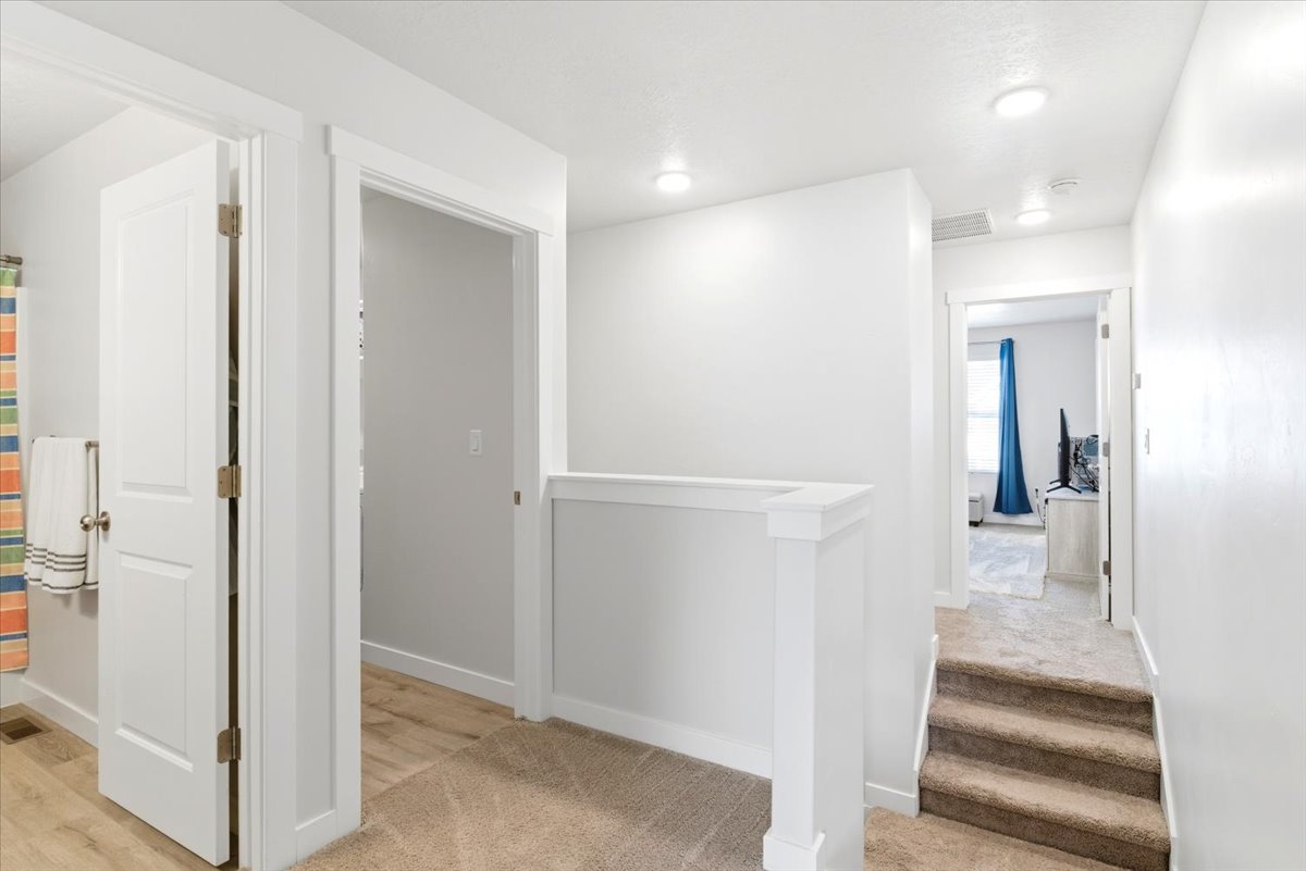 Upper-level landing featuring light-colored carpeting, white walls, recessed ceiling lighting, and a white balustrade