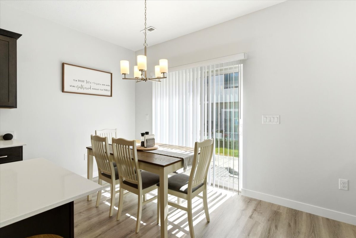 Dining area featuring wood-finish flooring, a contemporary chandelier, and a sliding glass door with vertical blinds