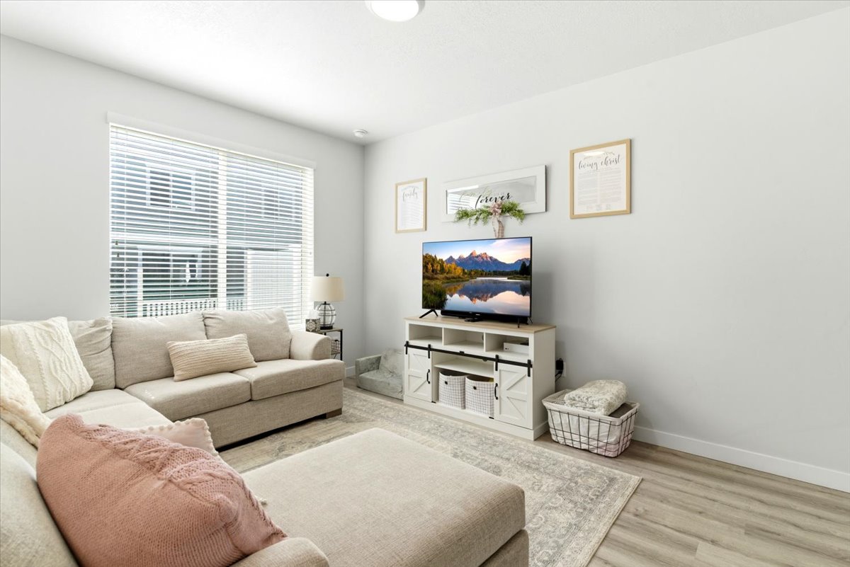Spacious living area featuring light-toned wood-finish flooring, a large window with blinds, and recessed lighting
