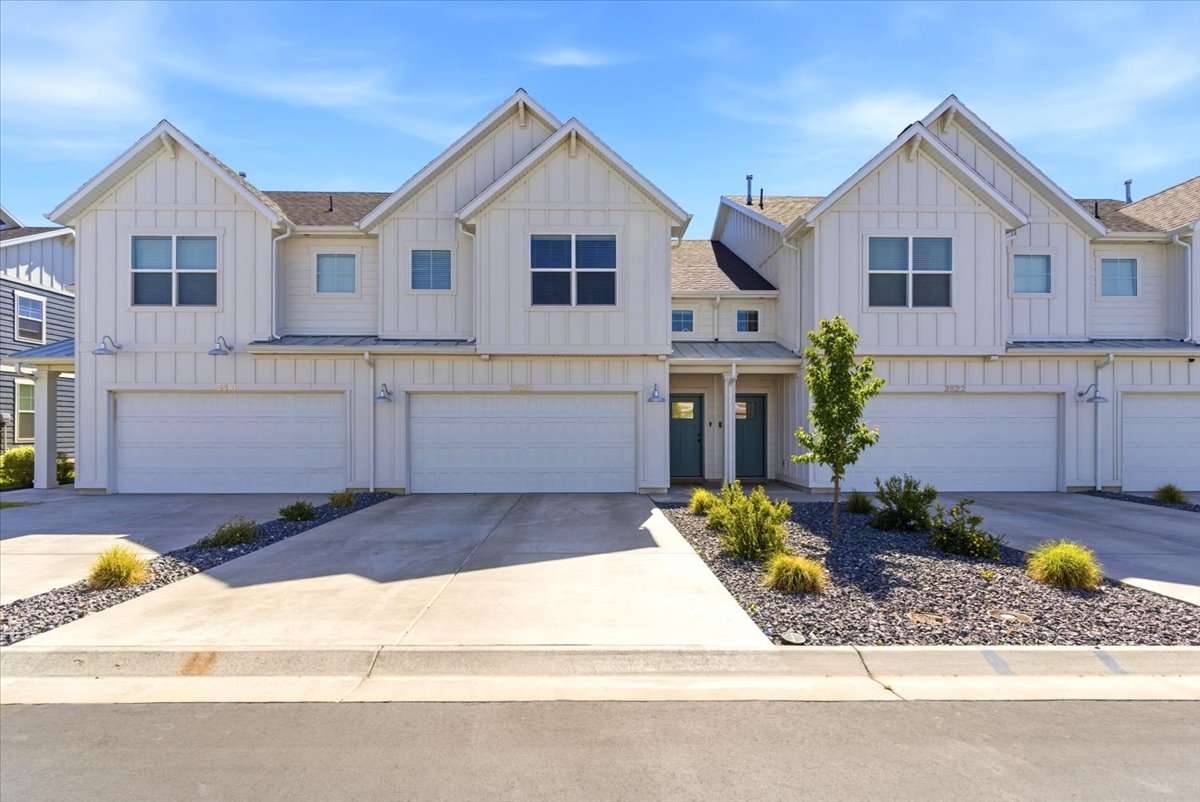 Modern farmhouse-style townhome featuring white vertical siding, prominent gables, and individual garages