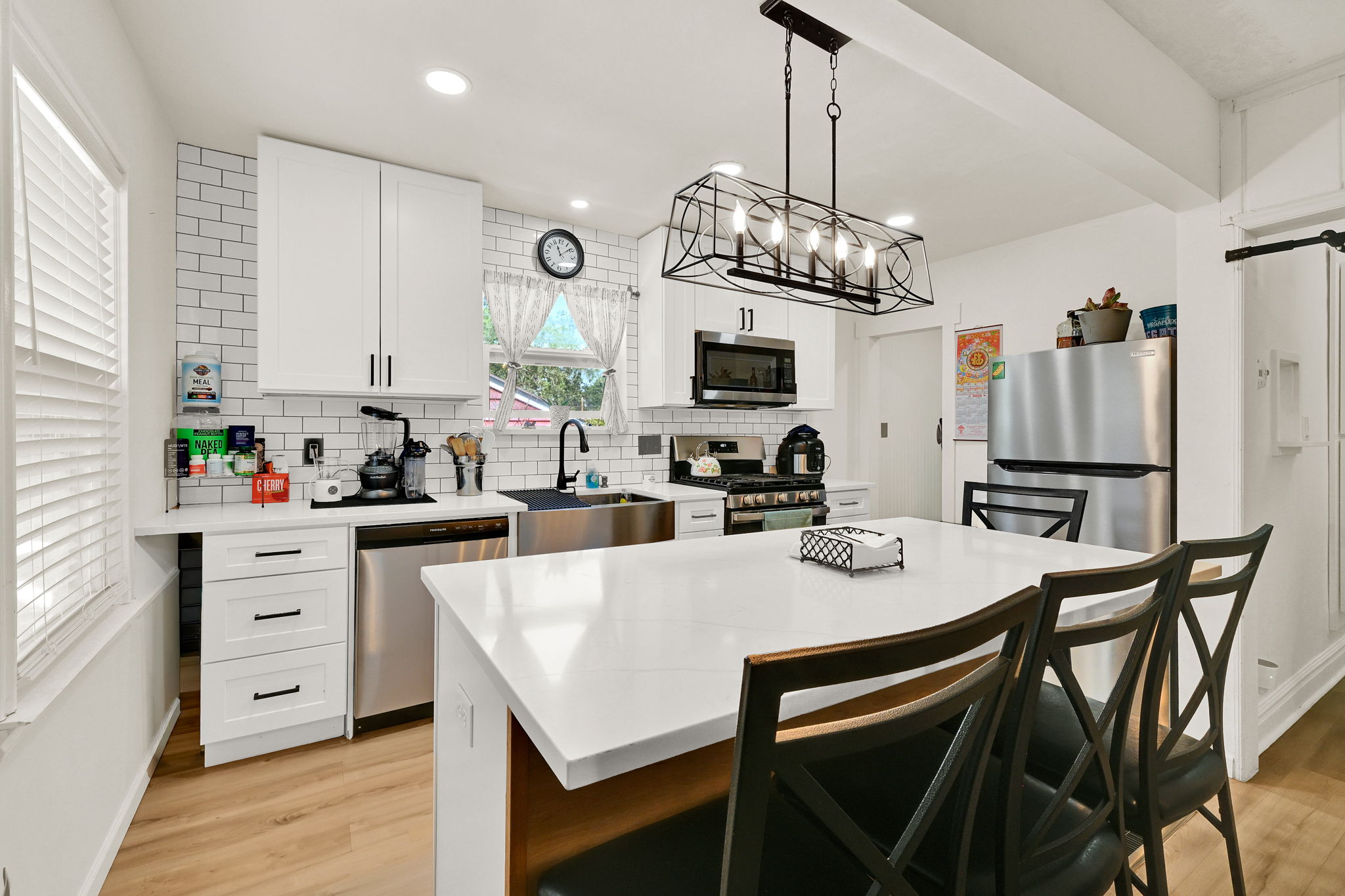 Bright kitchen featuring white cabinetry, subway tile backsplash, stainless steel appliances, a center island with seating, and wood-finish flooring