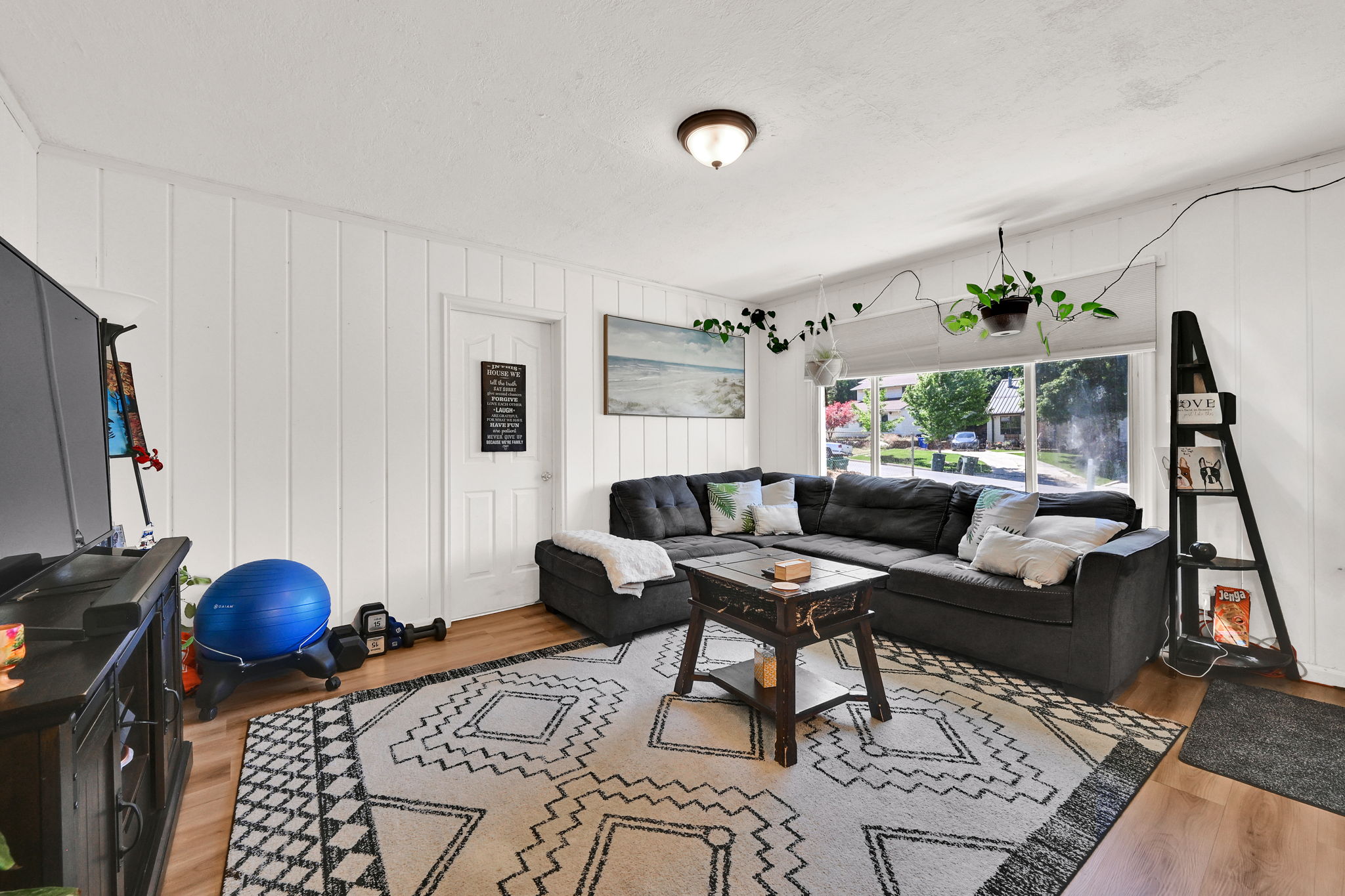 Open-concept living space featuring wood-finish flooring, white vertical wall paneling, and a large window