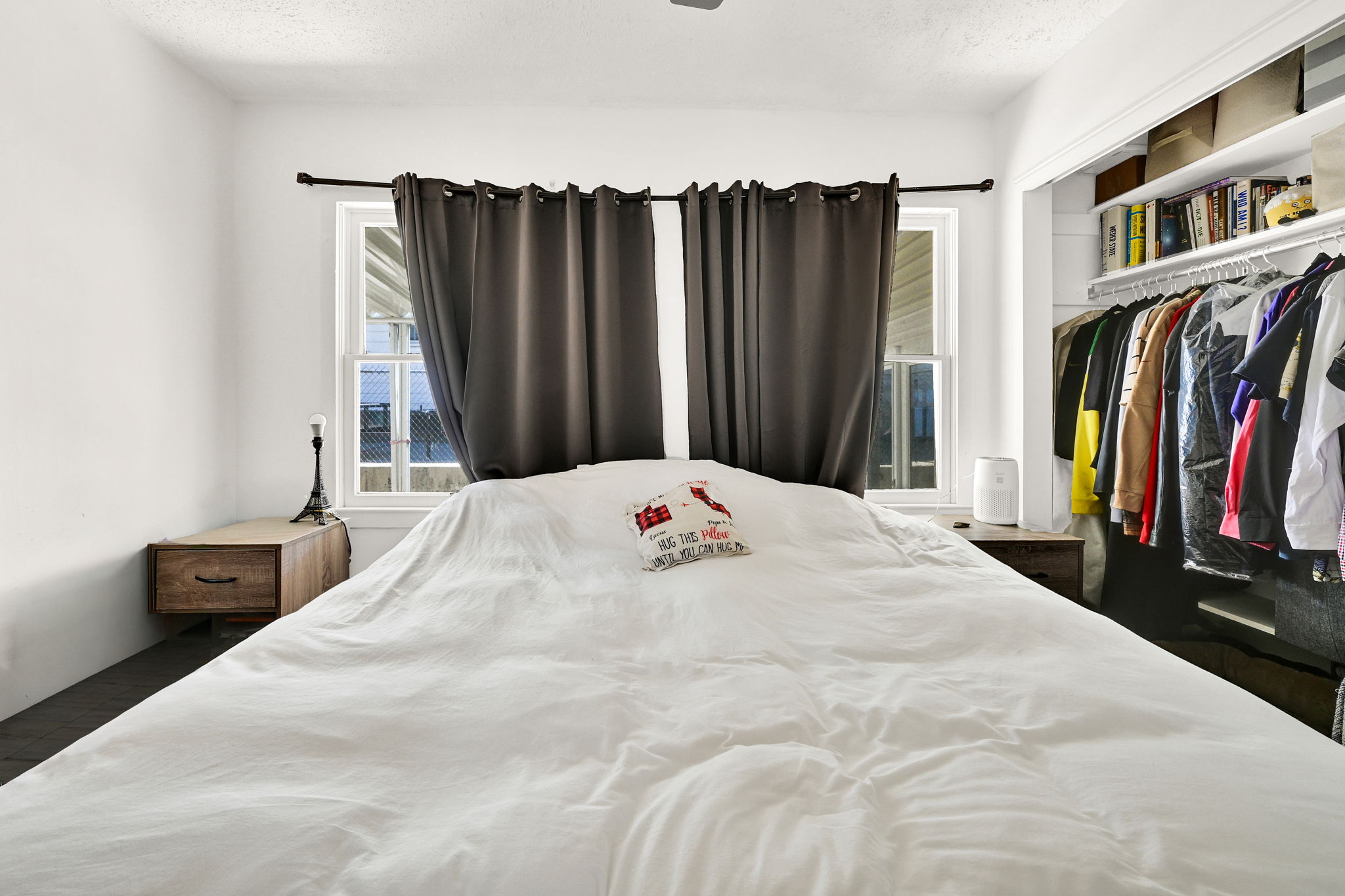 Bedroom featuring two windows with dark curtains, white walls, and dark flooring