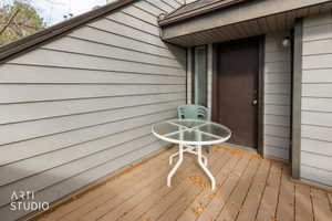 Exterior deck featuring wood-finish flooring, light gray horizontal siding, and a dark brown entry door