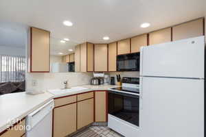 Kitchen featuring white appliances, recessed lighting, ample cabinetry, a built-in microwave, and a white sink