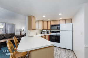Kitchen featuring herringbone-patterned tile flooring, recessed lighting, white appliances, and a breakfast bar