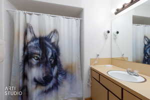 Bathroom featuring a single vanity with a laminate countertop, an integrated sink with a chrome faucet, and a large wall-mounted mirror with overhead bar lighting