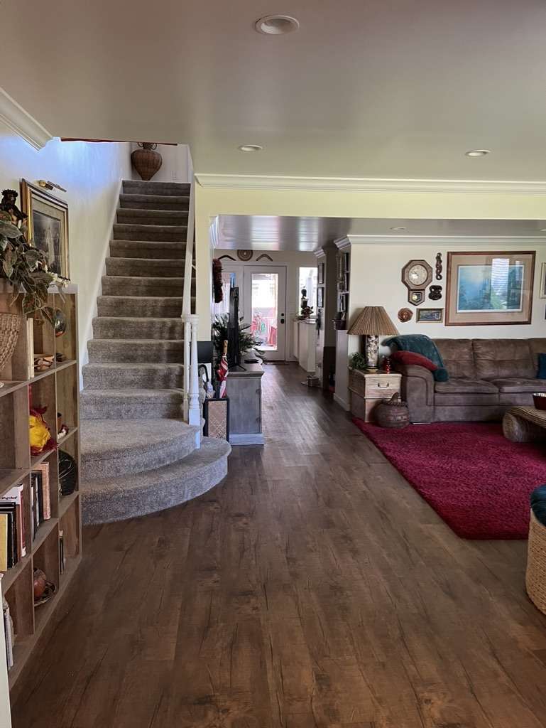Open-concept interior featuring wood-finish flooring, recessed lighting, crown molding, and a carpeted staircase with a rounded base