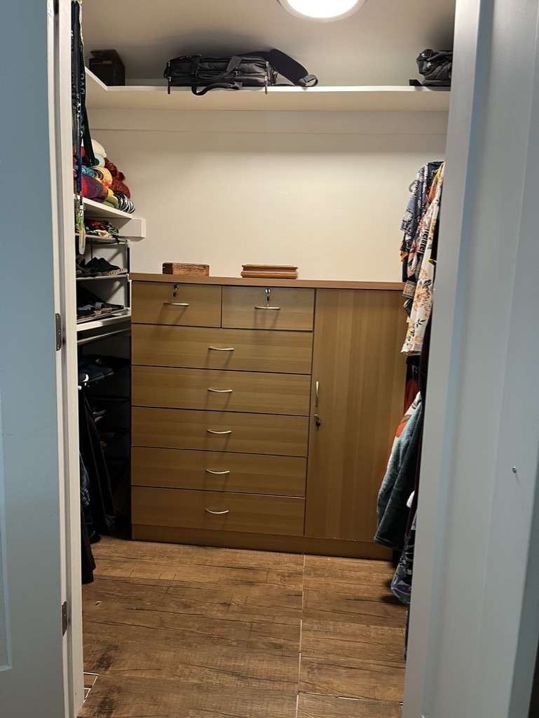 Custom closet system featuring wood-finish flooring, built-in drawers with metal hardware, and integrated shelving