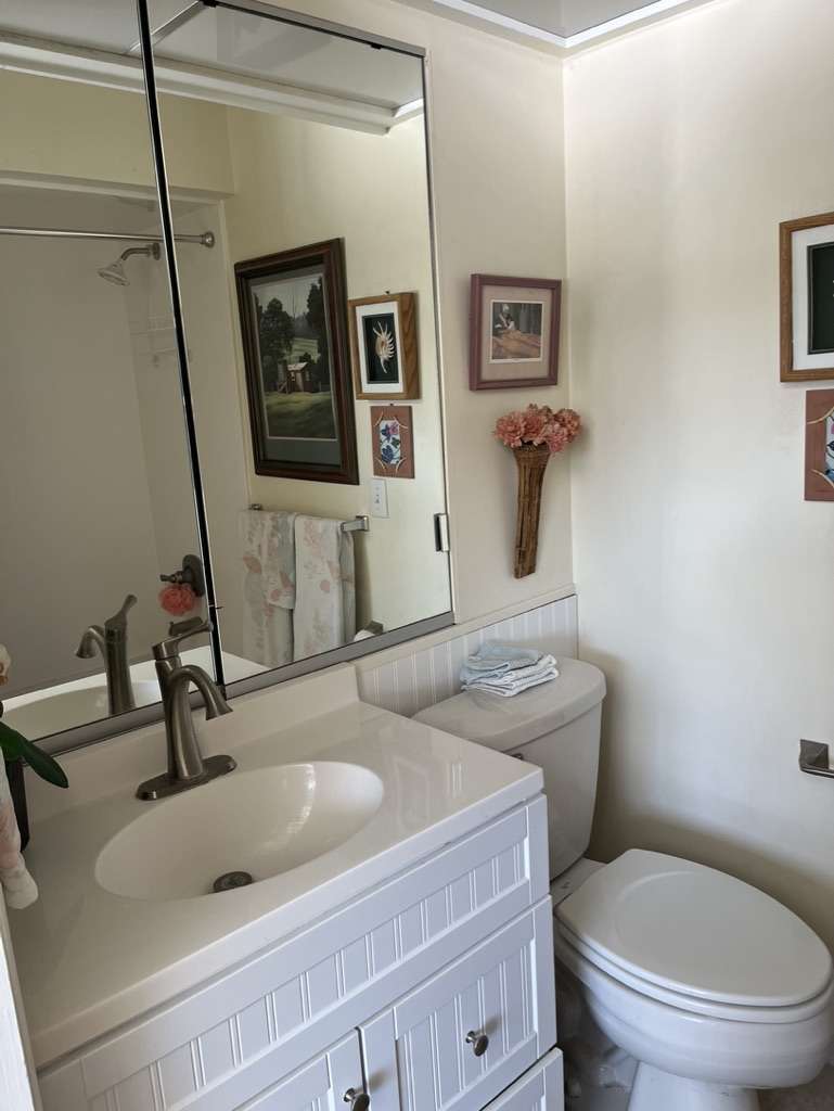 Bathroom featuring a white beadboard vanity with an integrated sink and brushed nickel faucet, a frameless wall-mounted mirror, and white wainscoting