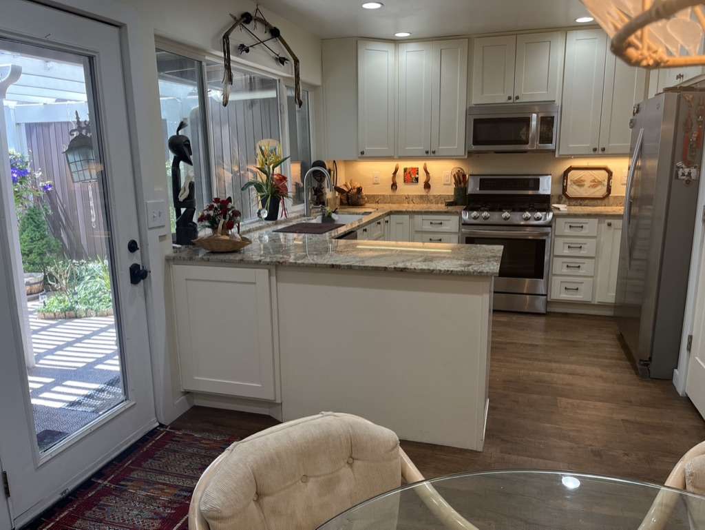 U-shaped kitchen featuring wood-finish flooring, white cabinetry, integrated stainless steel appliances, light-toned countertops, and a clear glass door providing access to the exterior