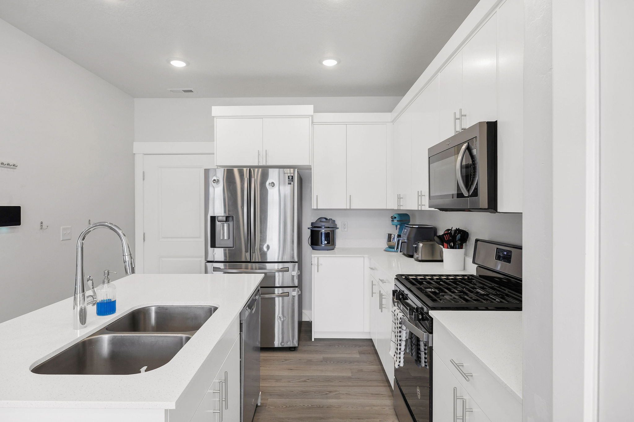 Modern kitchen featuring white cabinetry, a stainless steel refrigerator, stainless steel microwave, black gas range, and a kitchen island with a double basin sink