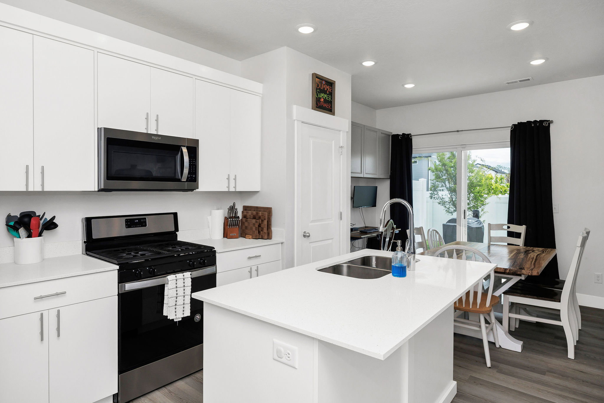 Modern kitchen featuring white cabinetry, a large kitchen island with an undermount double-basin sink, and stainless steel appliances including a gas range and microwave