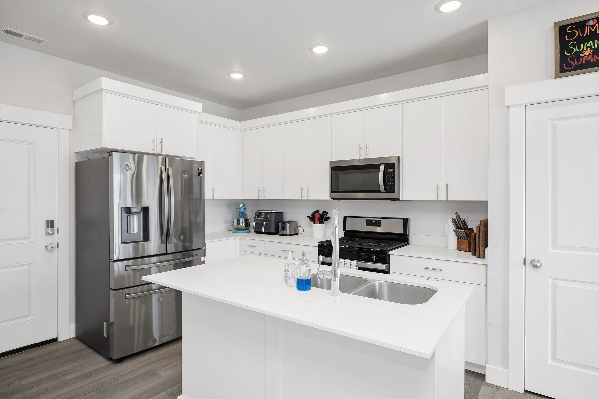 Contemporary kitchen featuring white cabinetry, stainless steel appliances, a center island with an integrated sink, white countertops, and recessed lighting