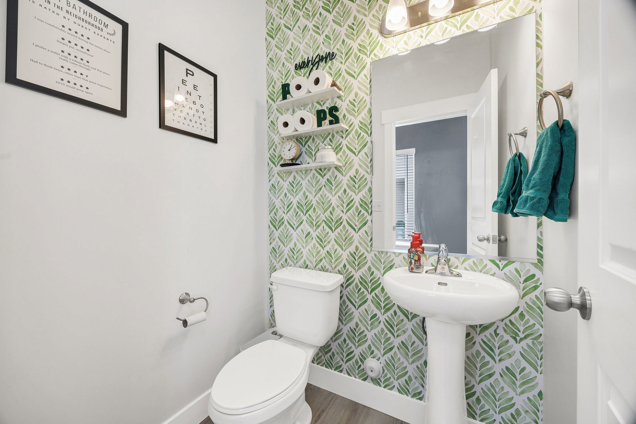 Pedestal sink with chrome faucet, complemented by a mirror and overhead vanity lighting