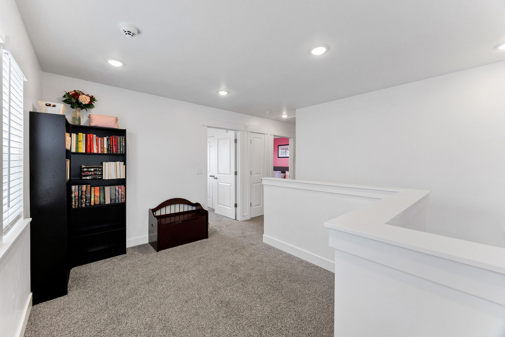 Carpeted open loft area featuring white walls and a white half-wall railing