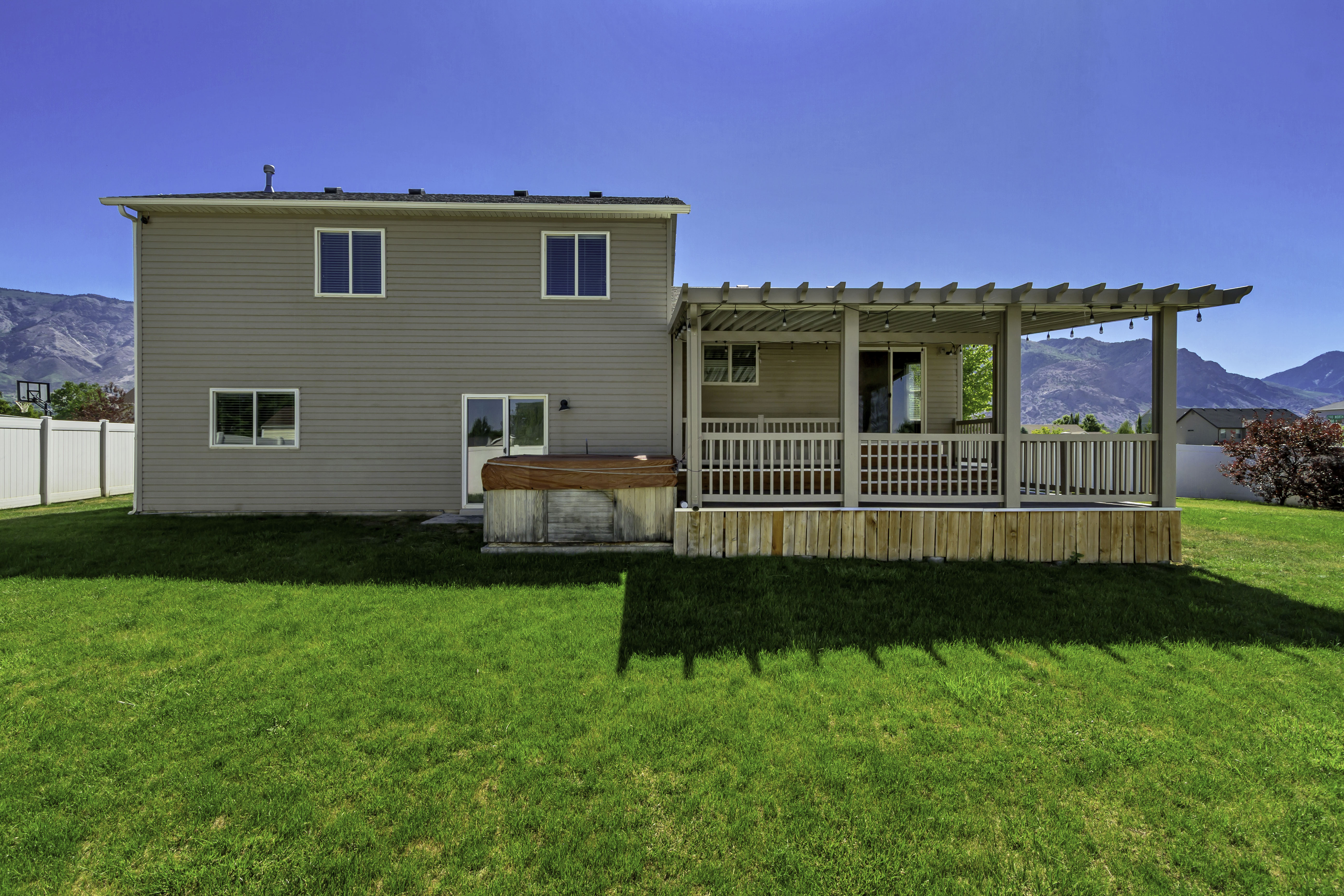 Rear exterior featuring a pergola-covered patio with string lighting, a hot tub, and a spacious lawn