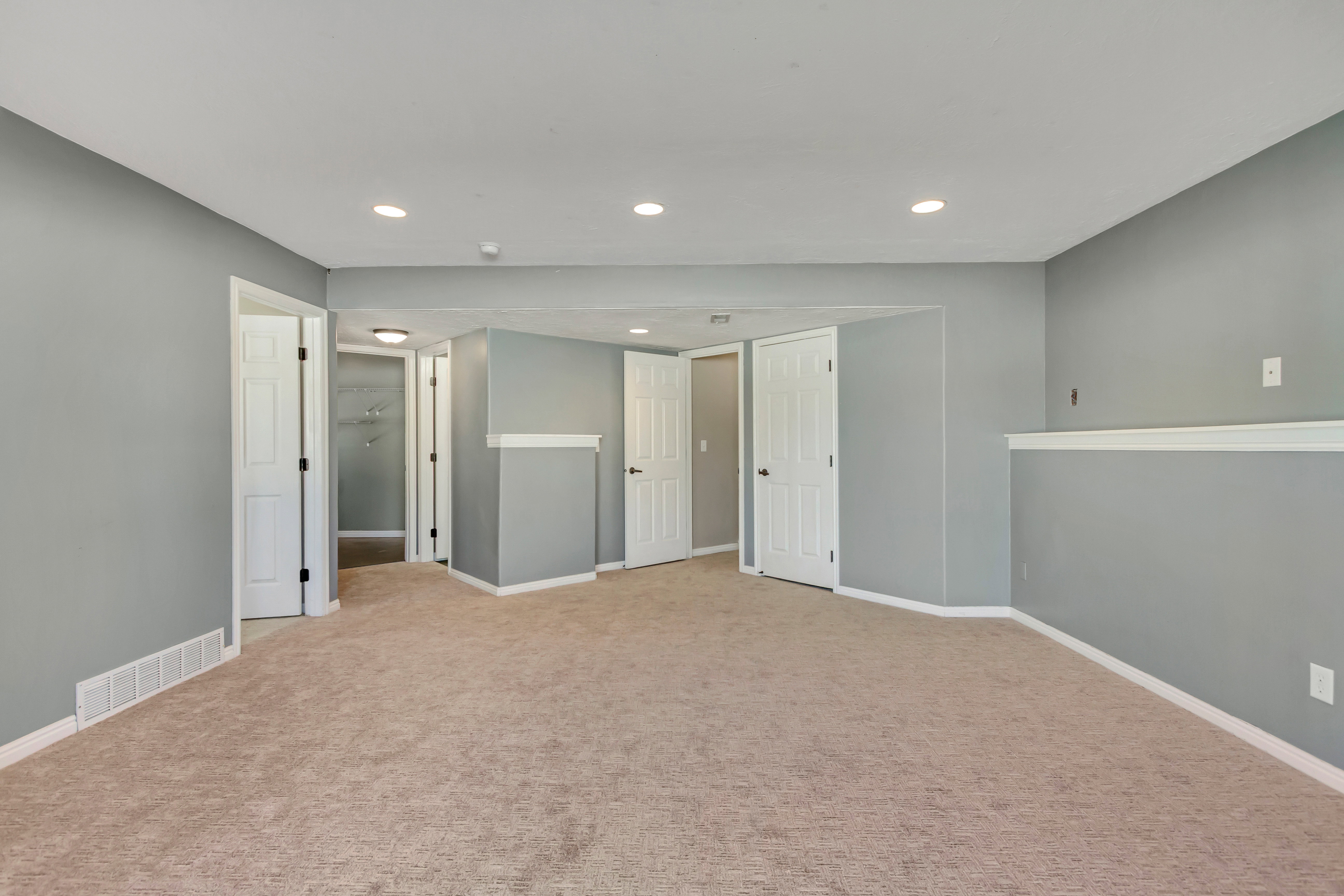 Spacious carpeted room featuring light gray walls, white trim, recessed lighting, and multiple white paneled doors