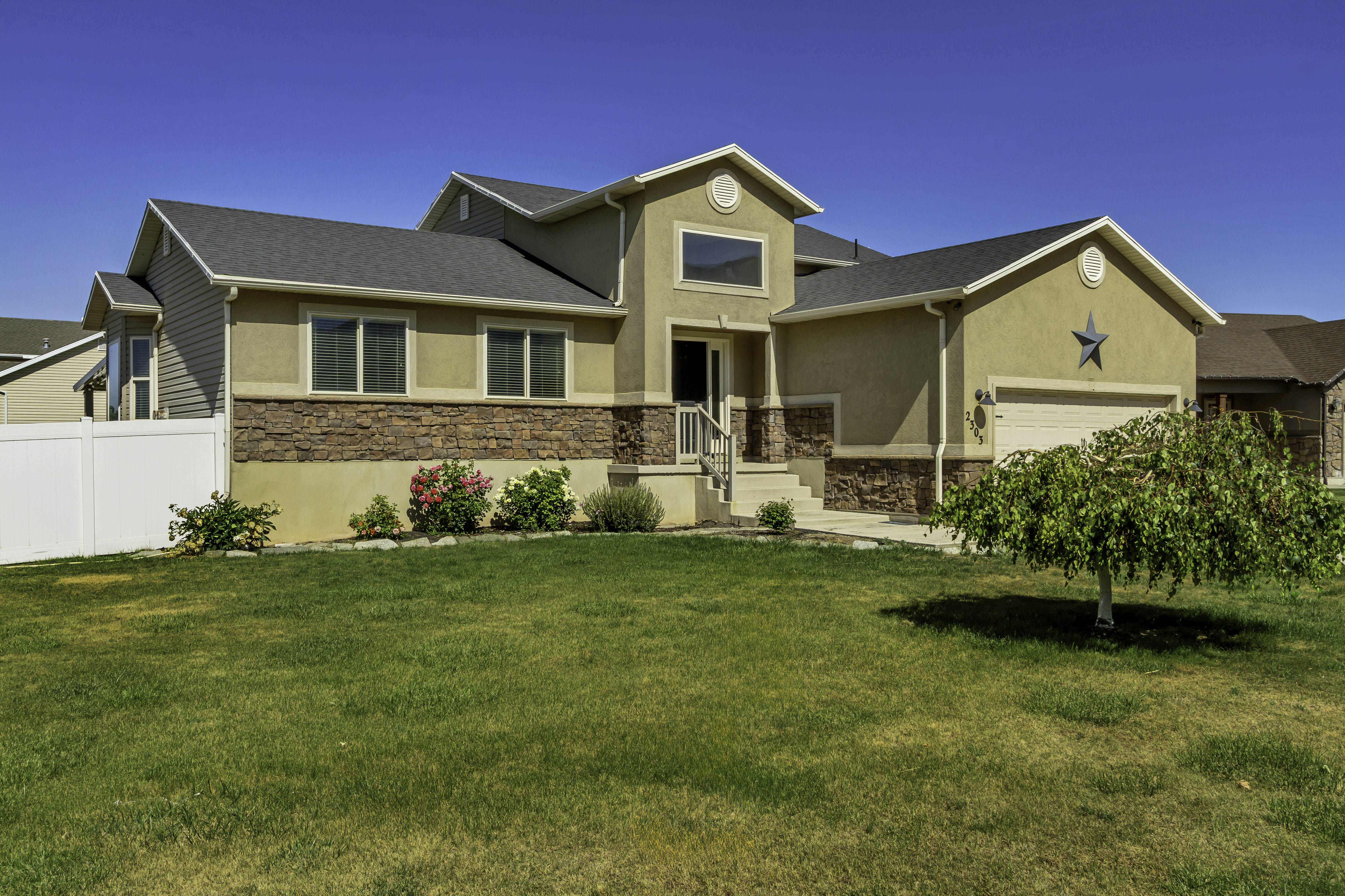 Stucco and stone facade home featuring a two-car garage, front entry stairs, and a partial white vinyl fence