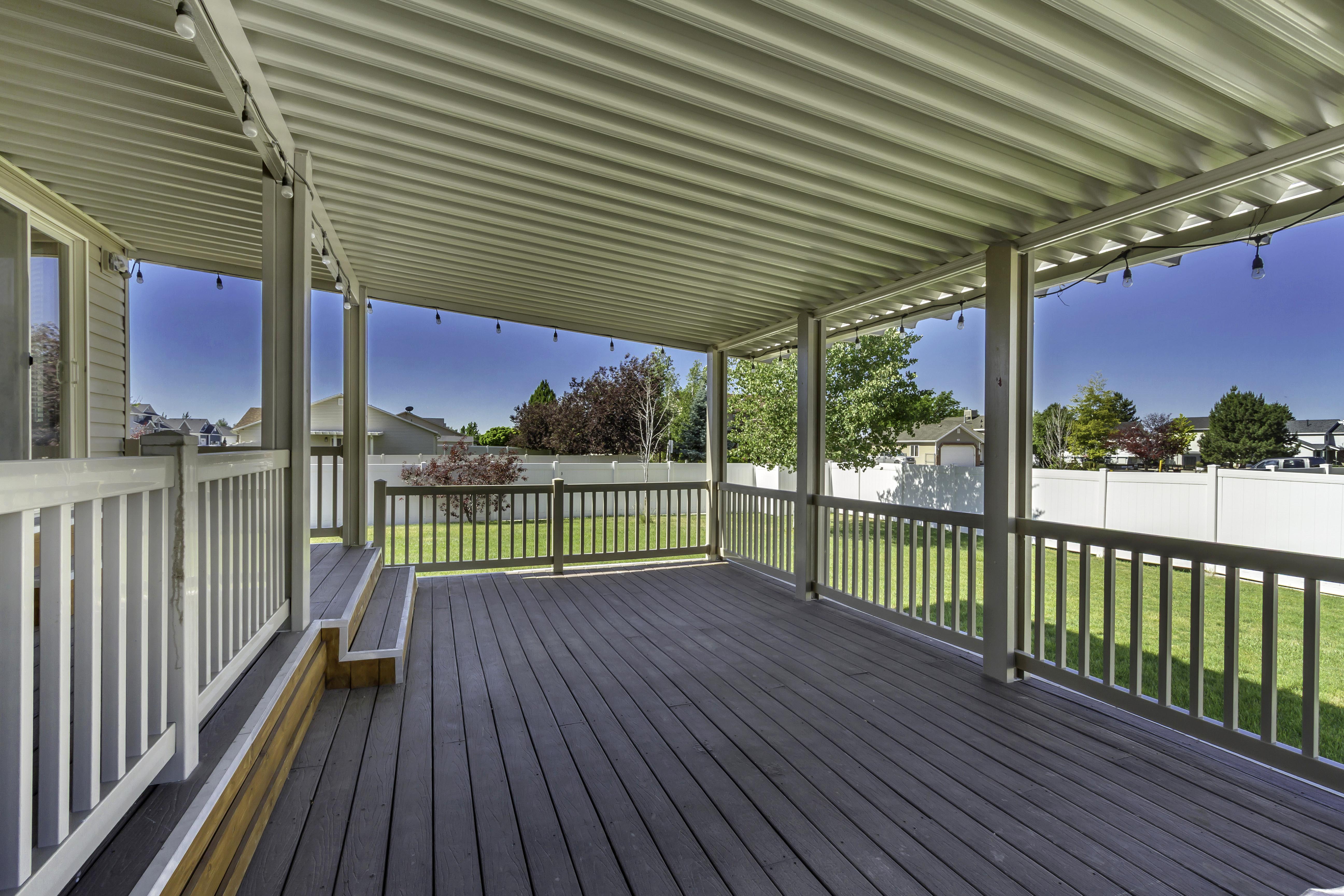 Spacious covered deck featuring composite decking, white railing, and a corrugated metal patio cover