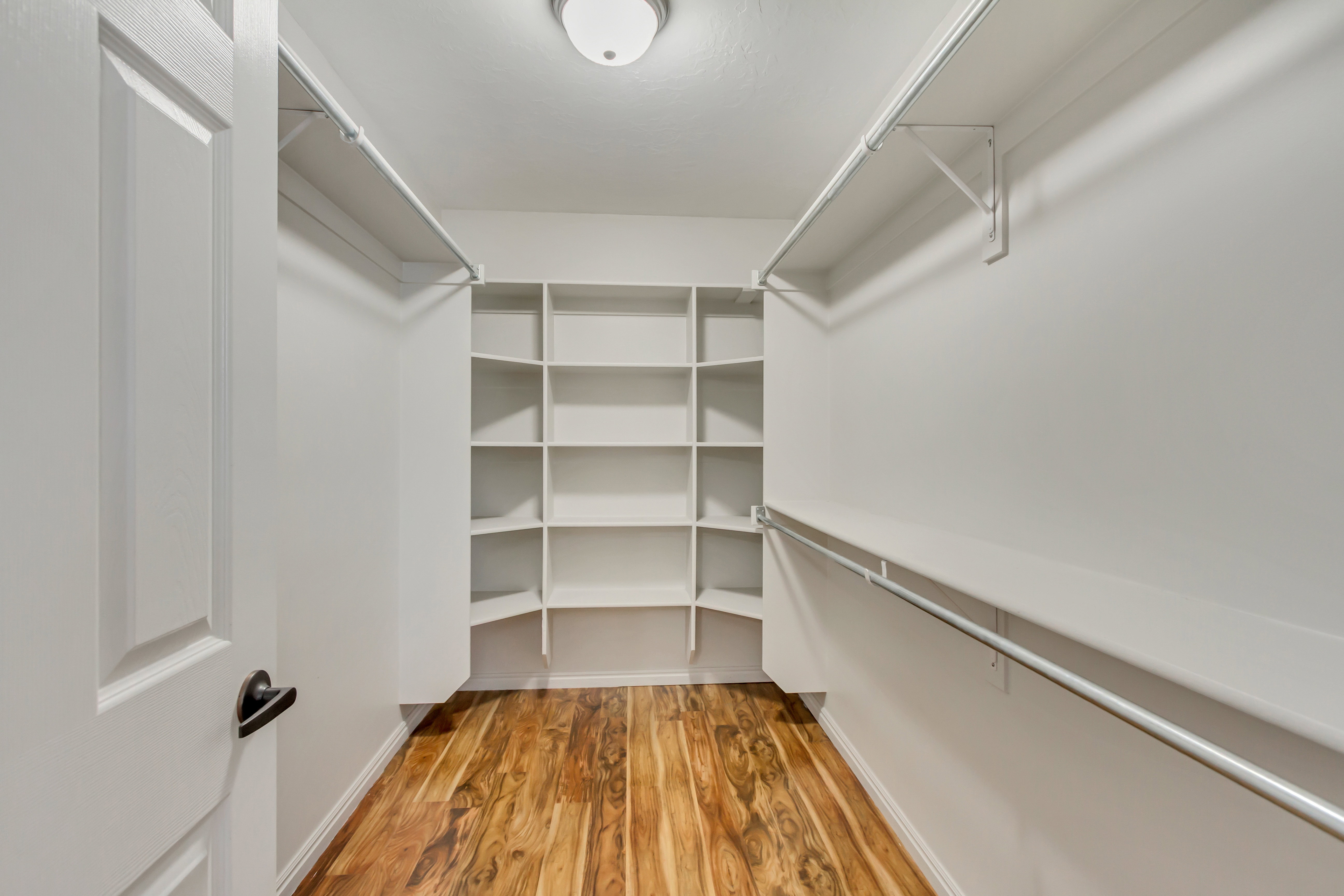 Walk-in closet featuring wood-finish flooring, white walls, built-in shelving, and multiple clothing rods