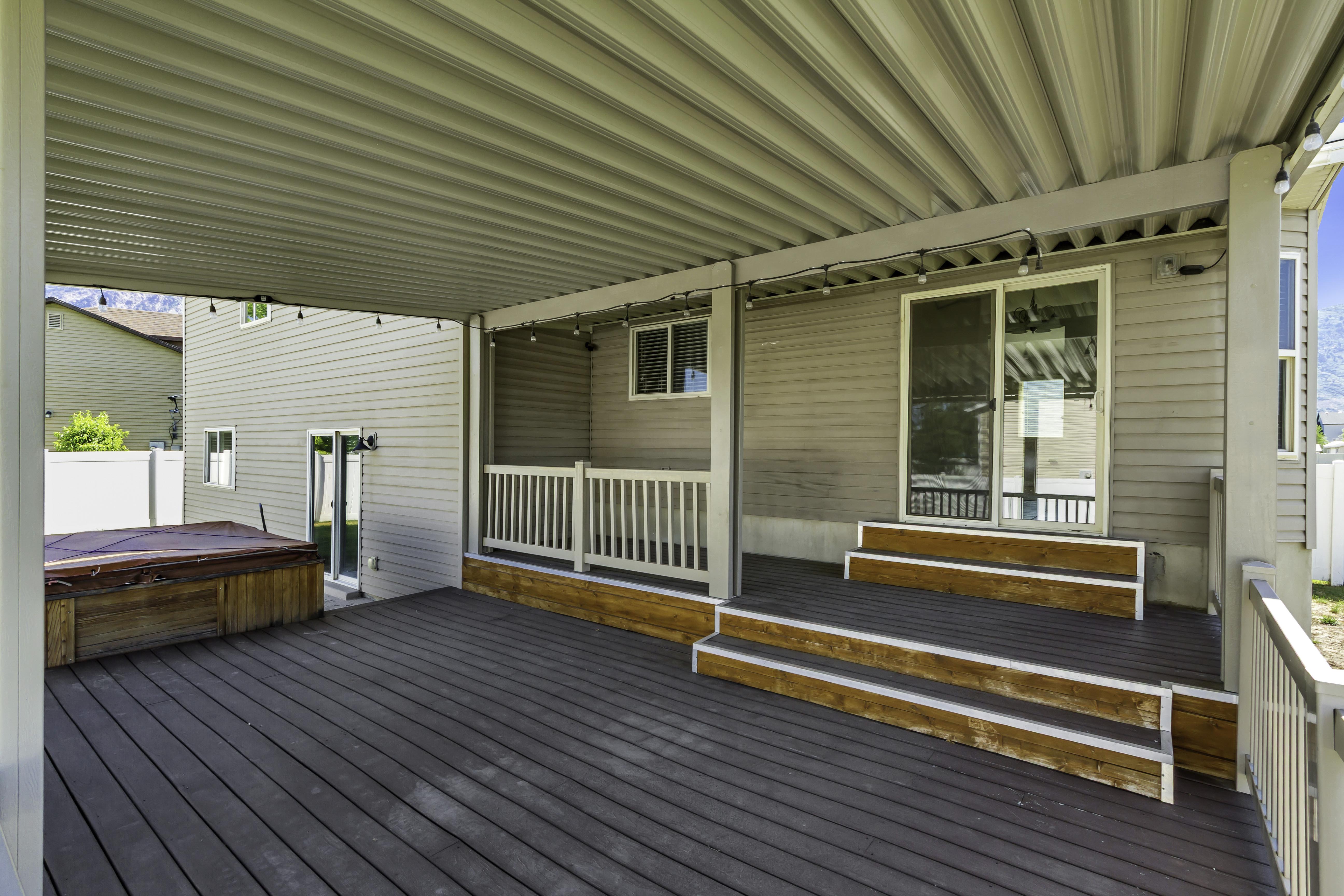 Expansive covered deck featuring composite decking, a built-in hot tub, and a sliding glass door entry