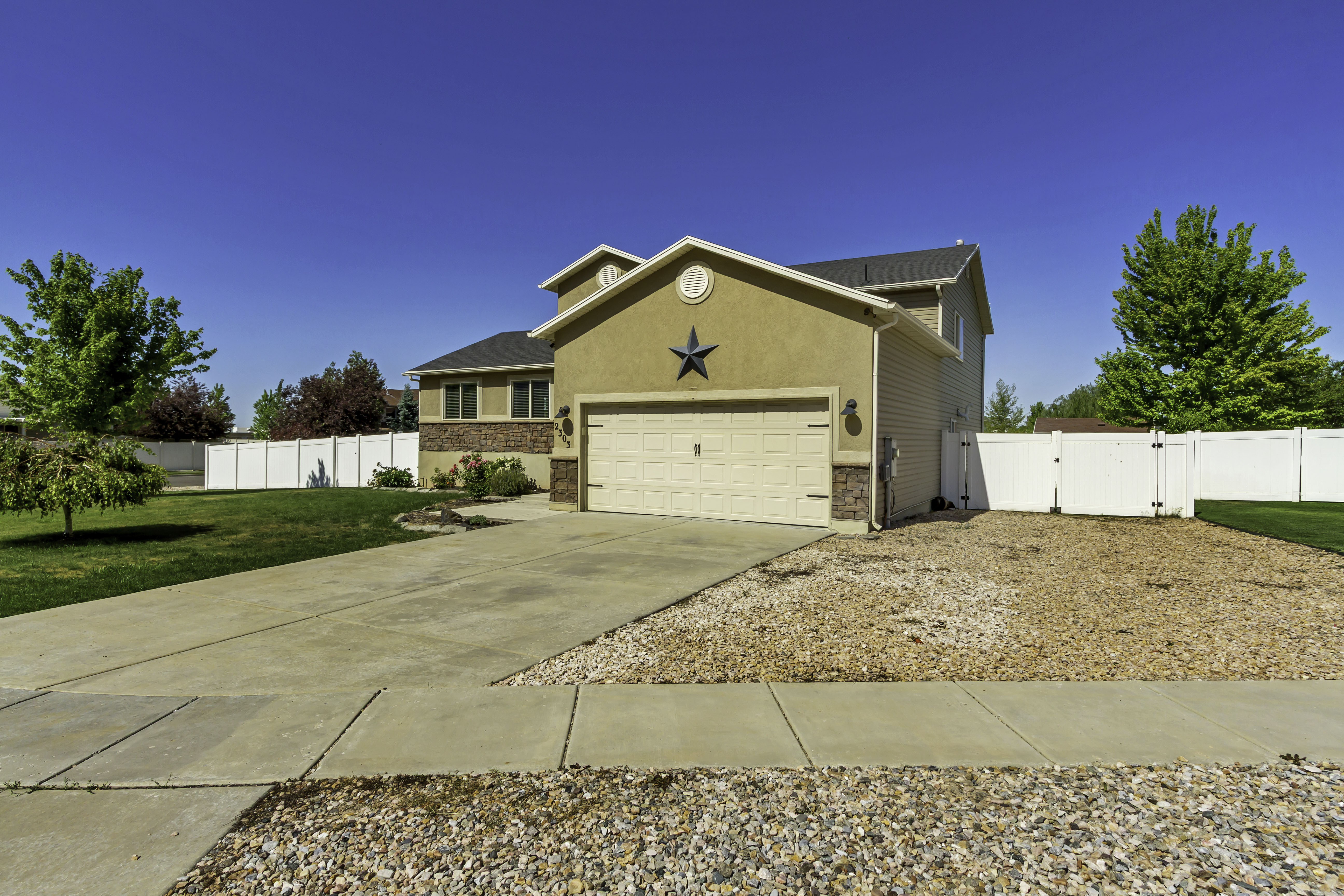 Stucco and stone facade home featuring an attached two-car garage with a panel door, a concrete driveway, and a white vinyl privacy fence enclosing the backyard
