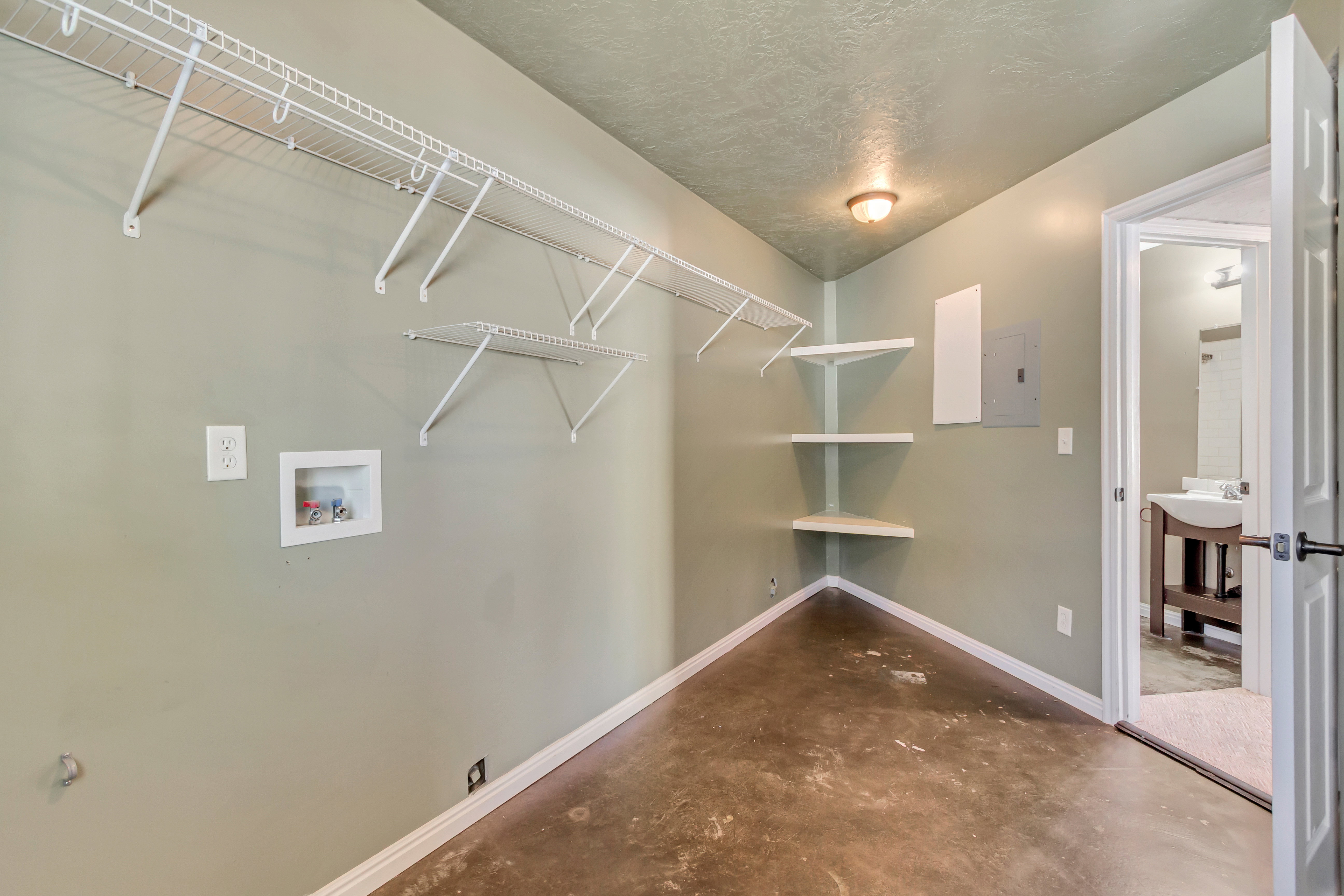Utility room featuring concrete flooring, wall-mounted wire shelving, corner shelves, a ceiling-mounted light fixture, and a laundry hookup