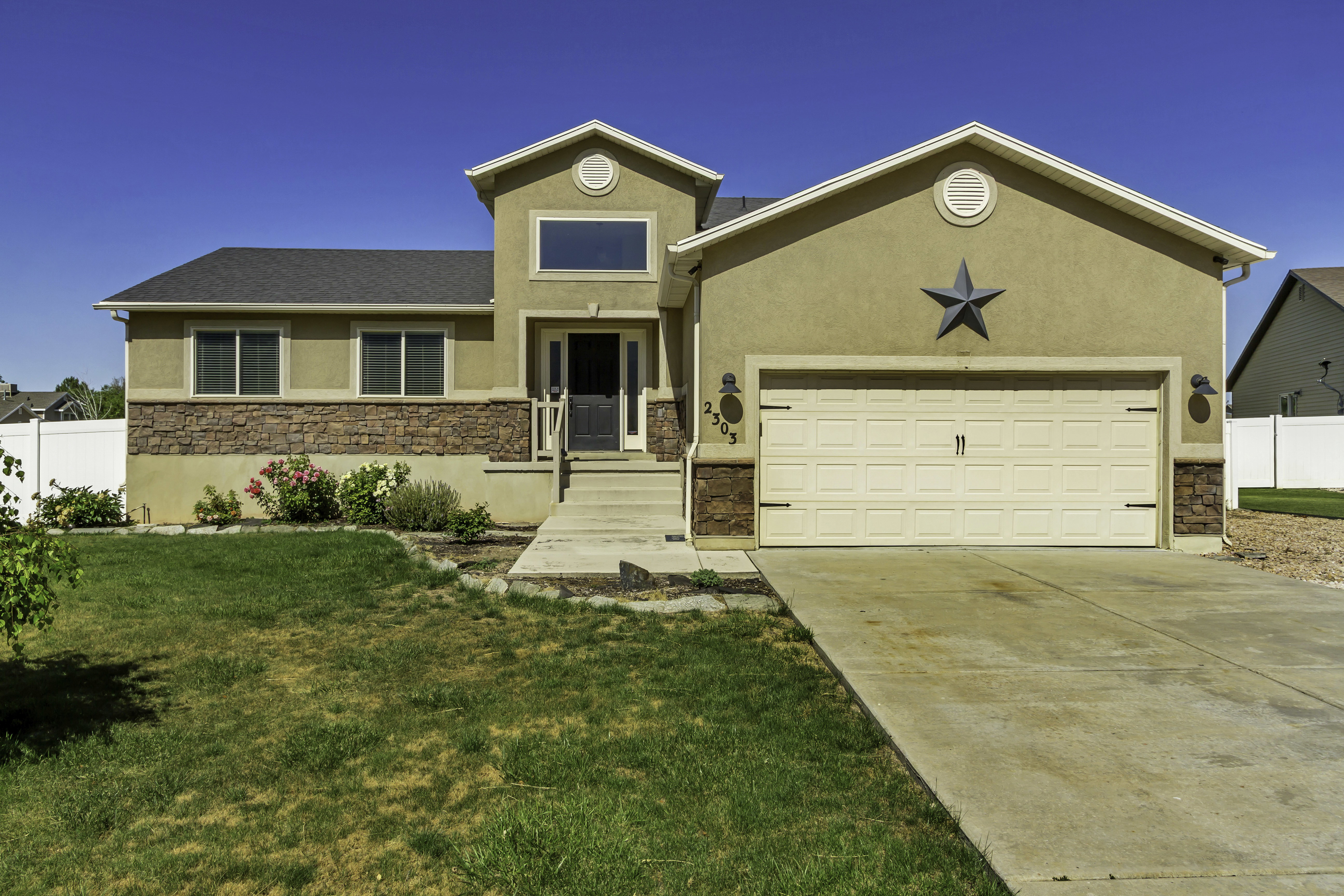 Stucco exterior featuring stone veneer accents, a two-car garage, and a concrete driveway